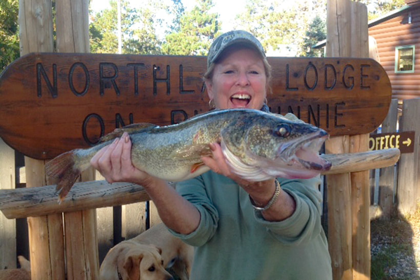 Woman holding large fish in front of Northland Lodge sign